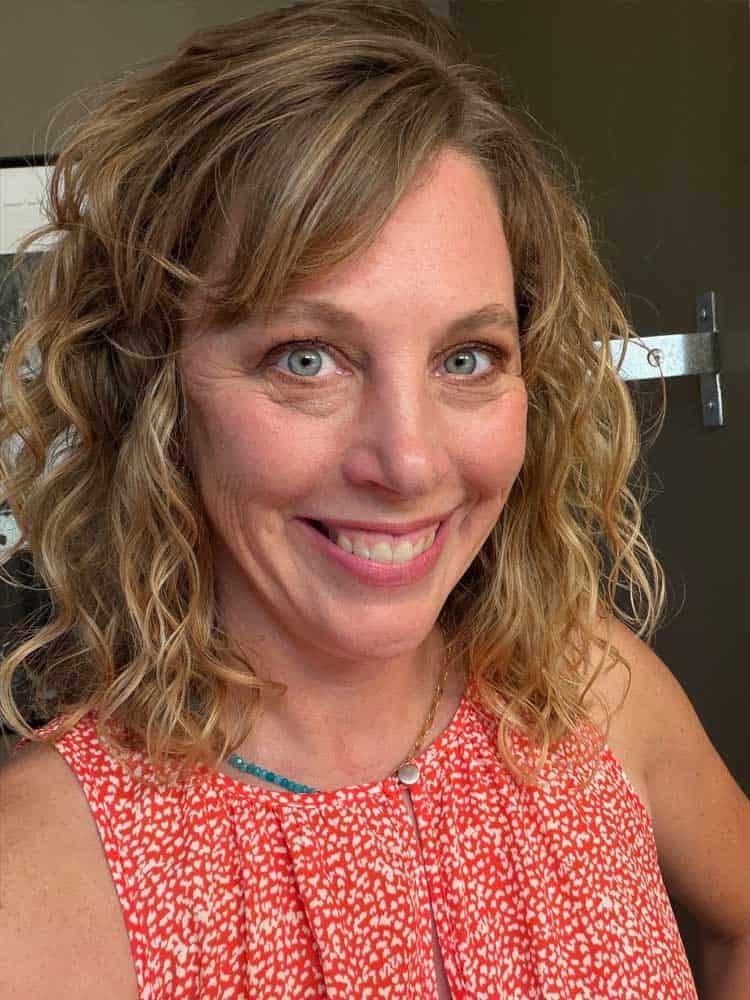 After color analysis, the same woman wearing a warm, vibrant red-orange top, with brighter-looking skin and eyes and a more balanced overall appearance.